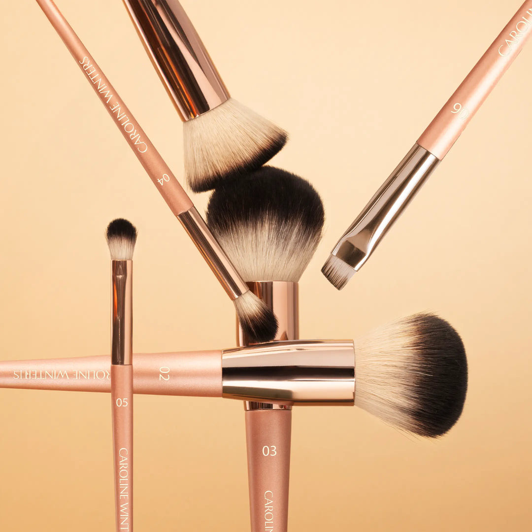 Set of makeup brushes with rose gold handles on a beige background
