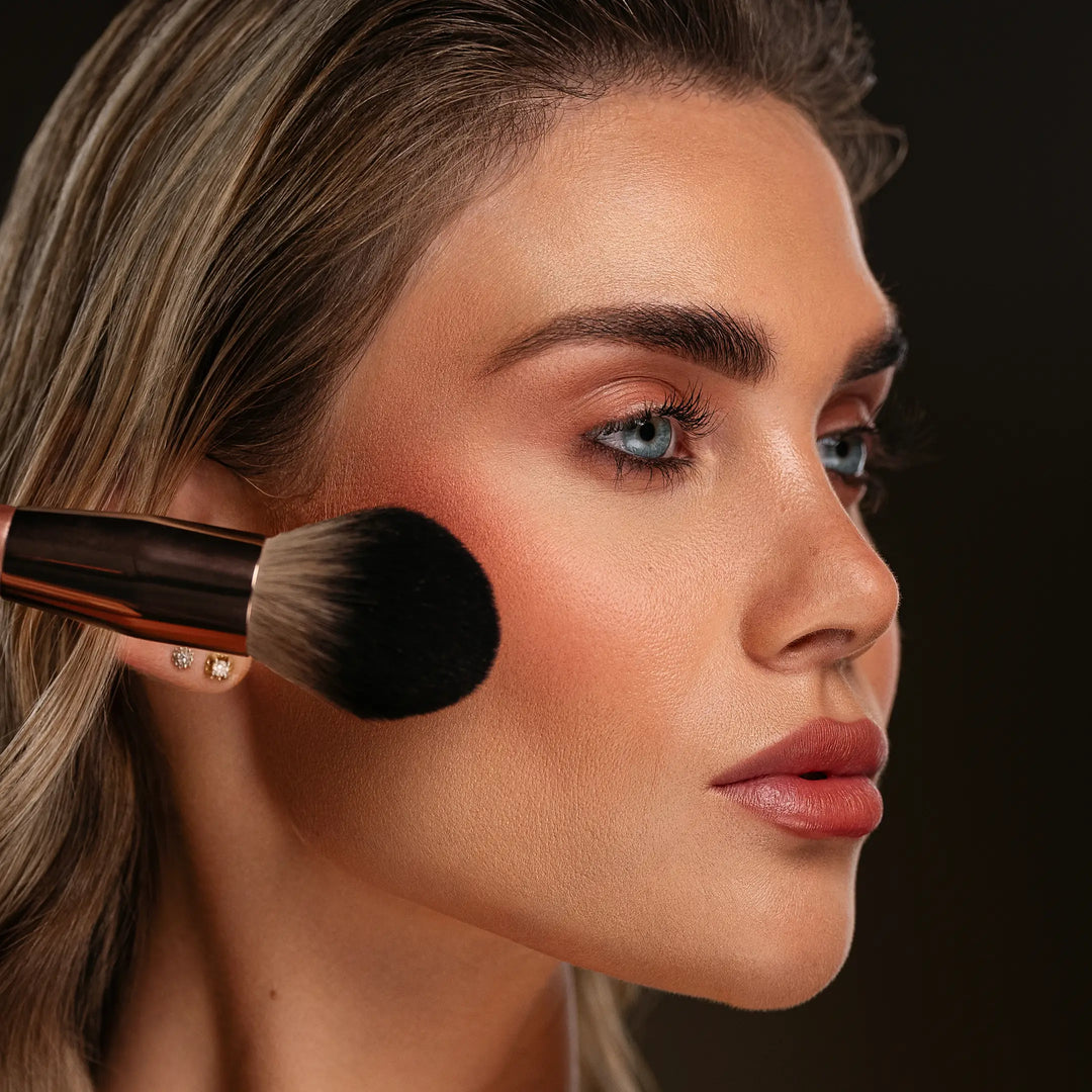 Woman applying makeup with a brush on a dark background