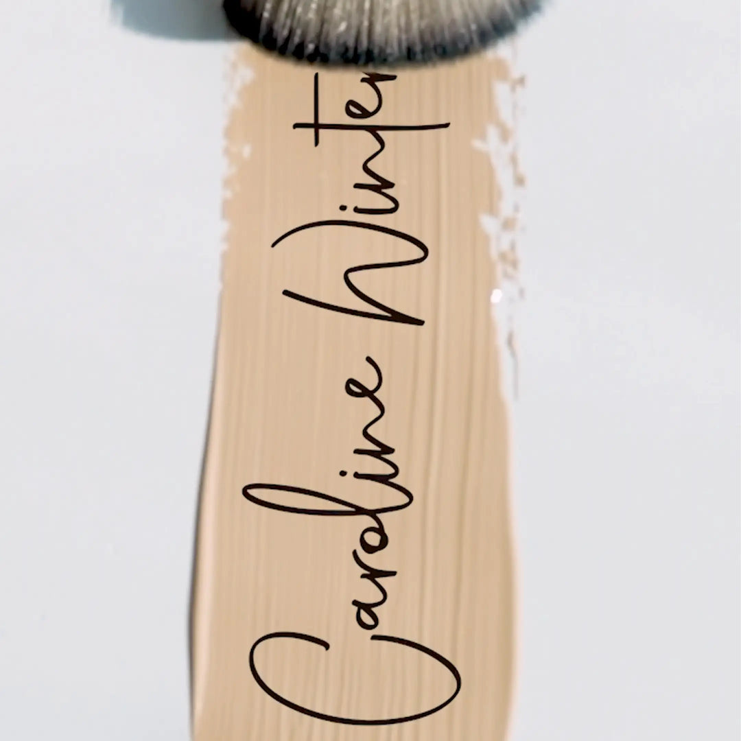 Makeup brush with Caroline Winter branding on a light background